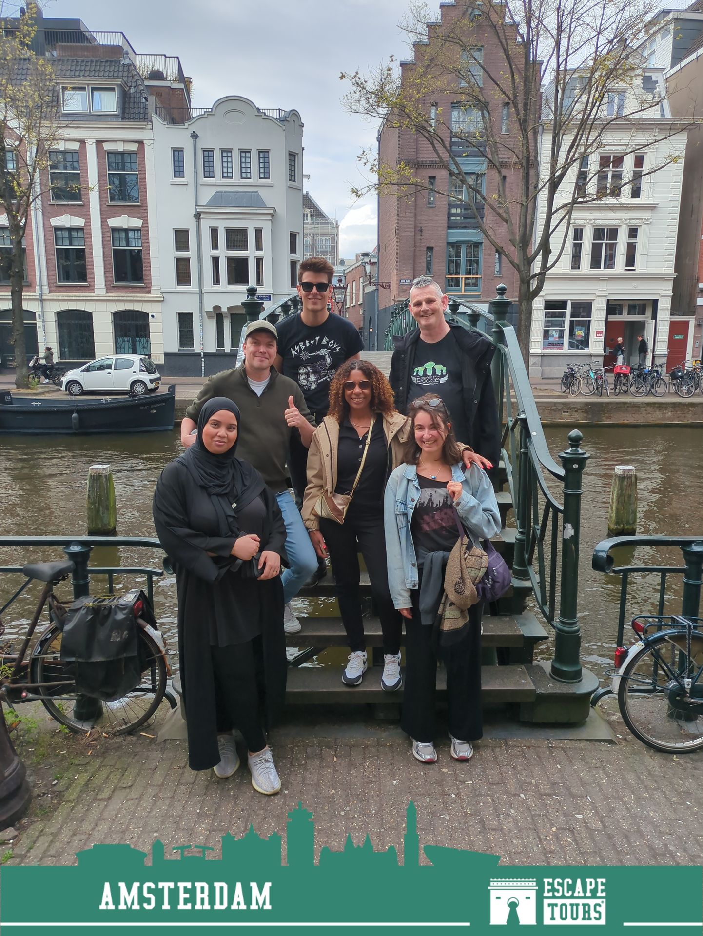 Groep van zes personen poseren samen op een steiger aan een kanaal met historische gebouwen op de achtergrond