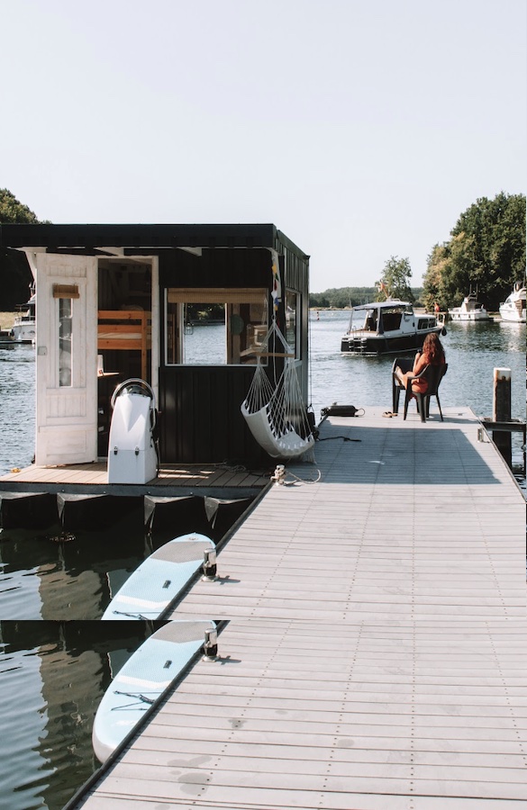 Zwart-wit tiny house op een steiger aan het water met hangmatten en zicht op boten in de haven