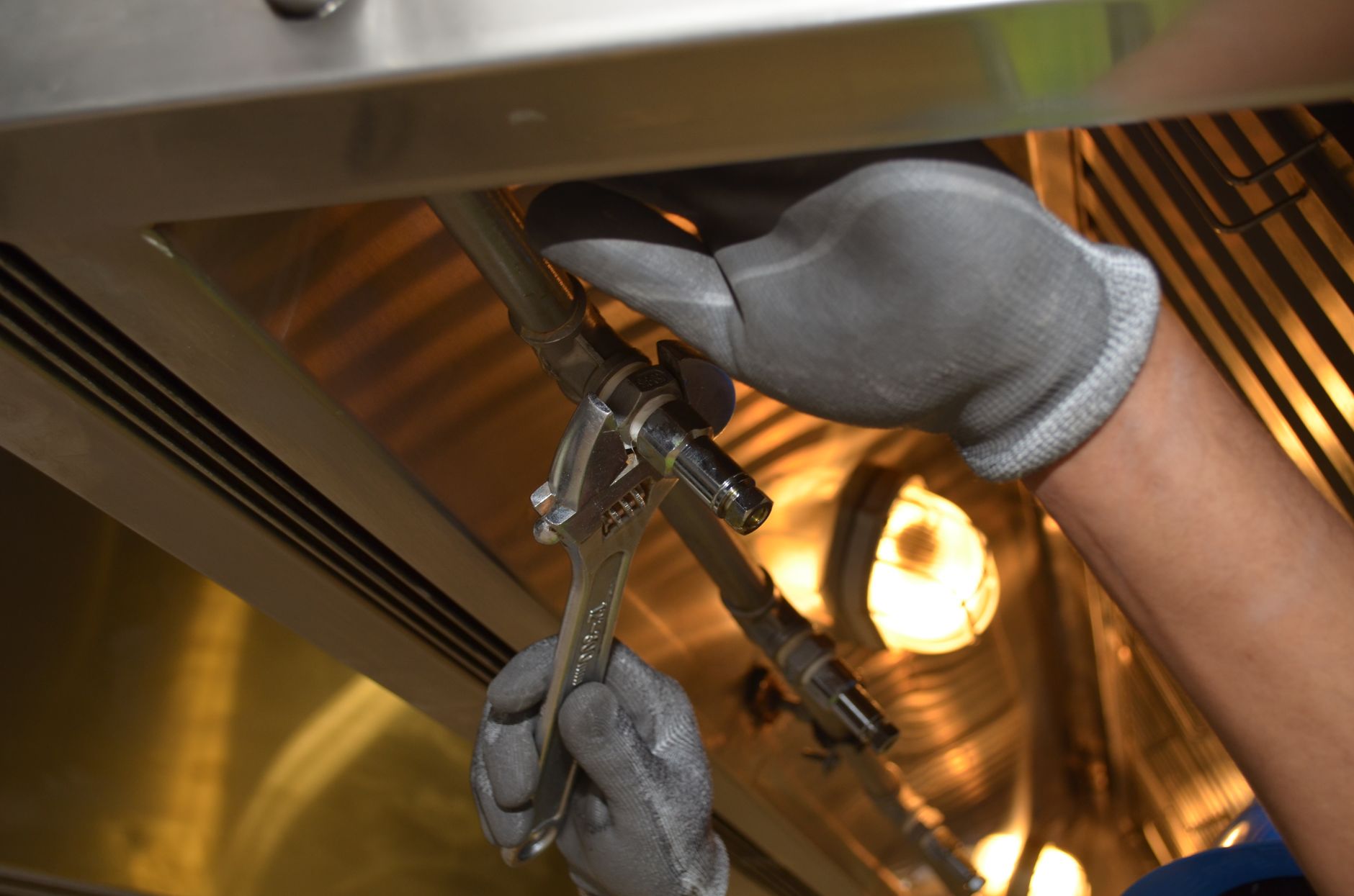 Handen met werkhandschoenen monteren een kraan onder een wastafel bij warm licht.